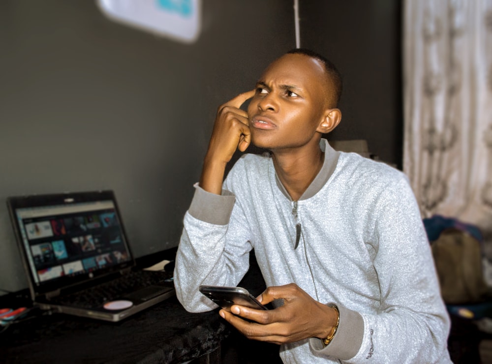 a man sitting in front of a laptop and holding a cell phone