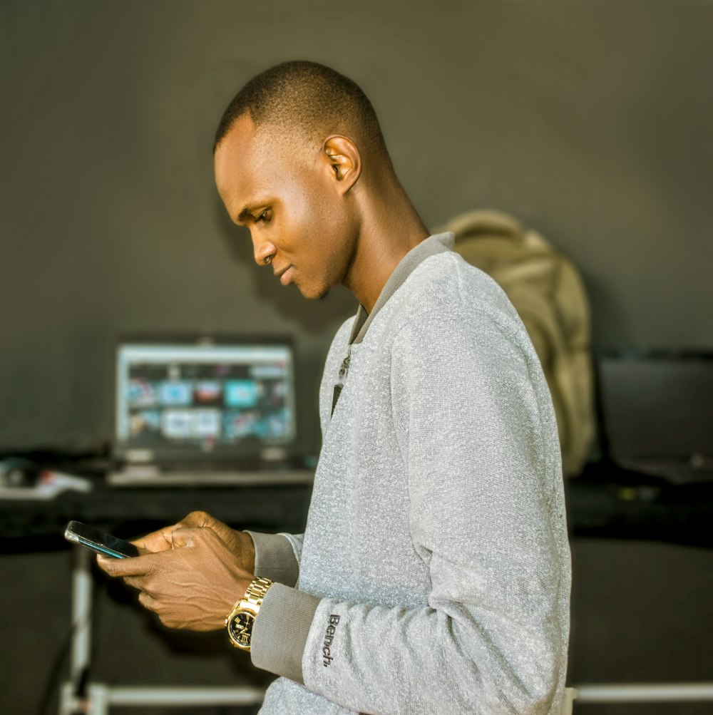 Ein Mann steht vor einem Laptop und hält ein Handy in der Hand