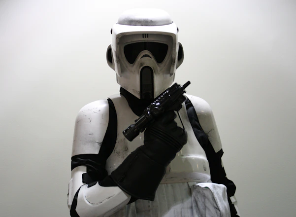 A person wearing a detailed, futuristic white and black armored suit with a helmet, holding a weapon in a defensive or ready stance.
