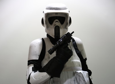 A person wearing a detailed, futuristic white and black armored suit with a helmet, holding a weapon in a defensive or ready stance.