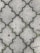 Interlocking concrete tiles create a geometric pattern on a walkway. The tiles have a light gray color, and small patches of green moss grow in the gaps between them. The surface of the tiles appears worn, with slight discolorations and spots visible.