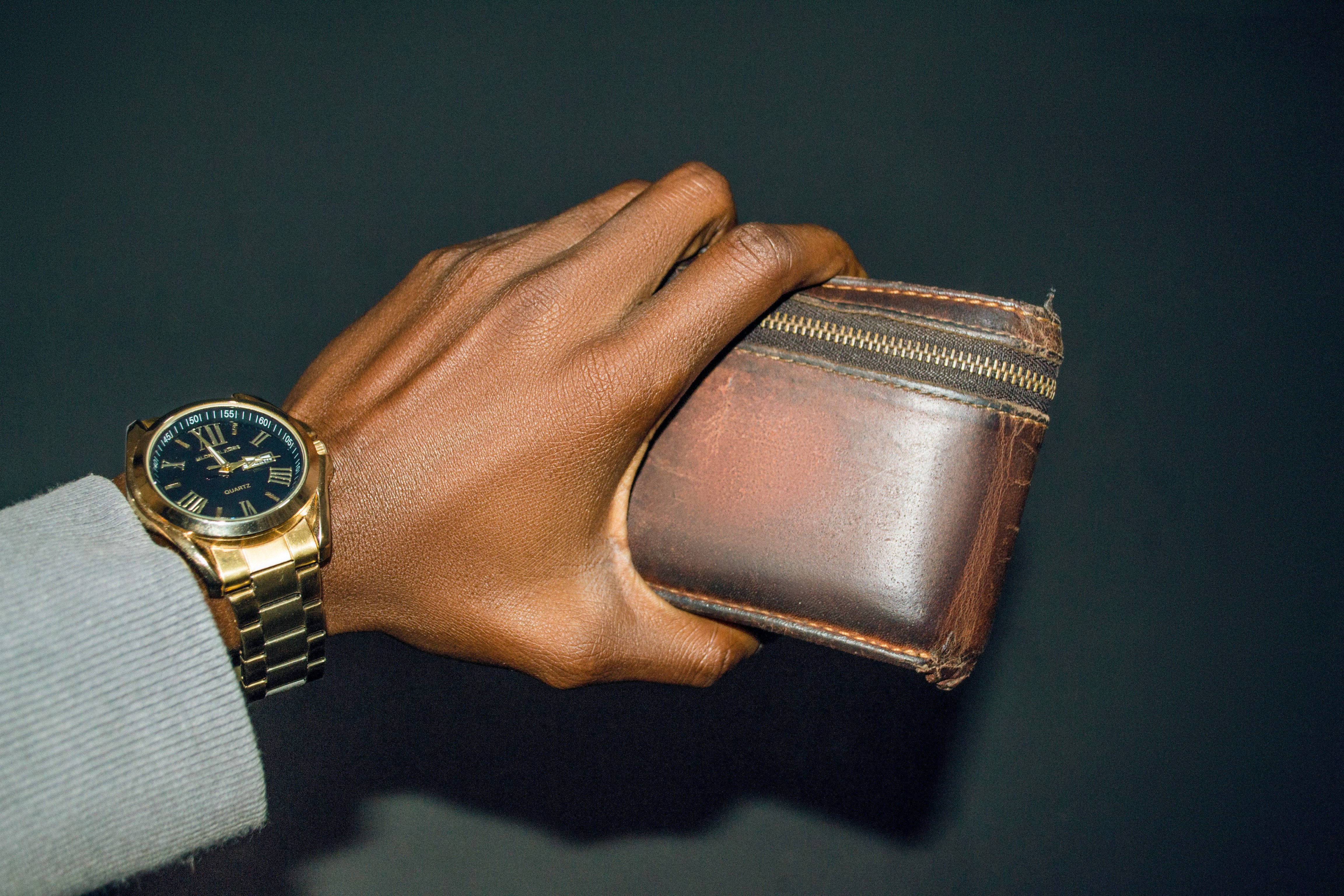 a hand with a wristwatch holding a brown leather wallet or purse