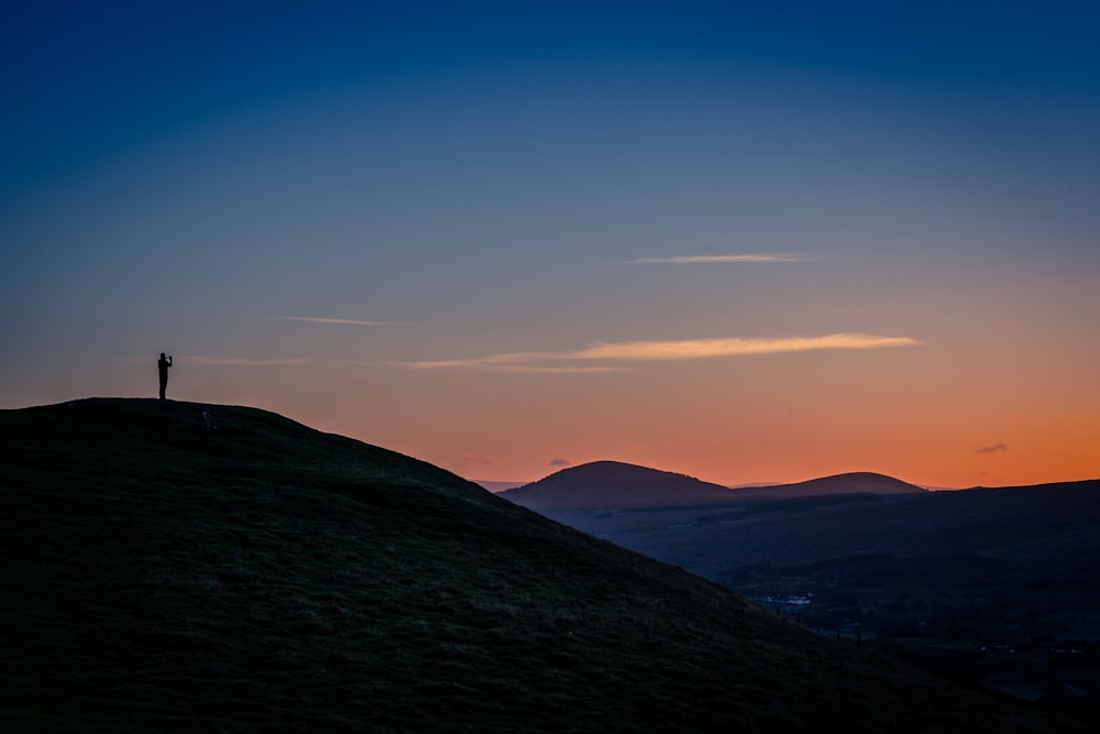 una persona in piedi sulla cima di una collina al tramonto