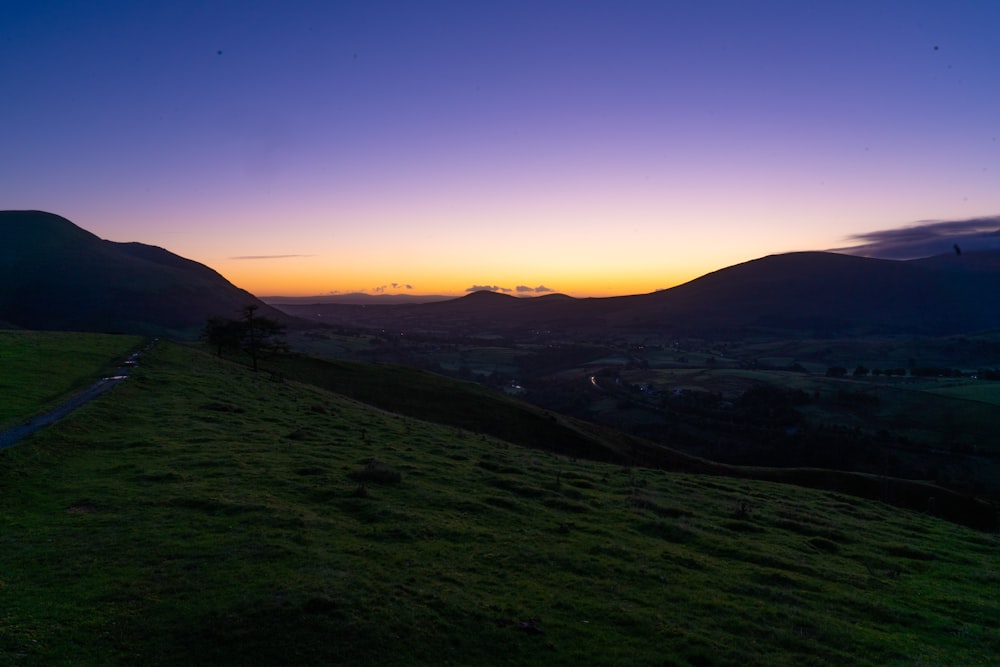 the sun is setting over a grassy hill