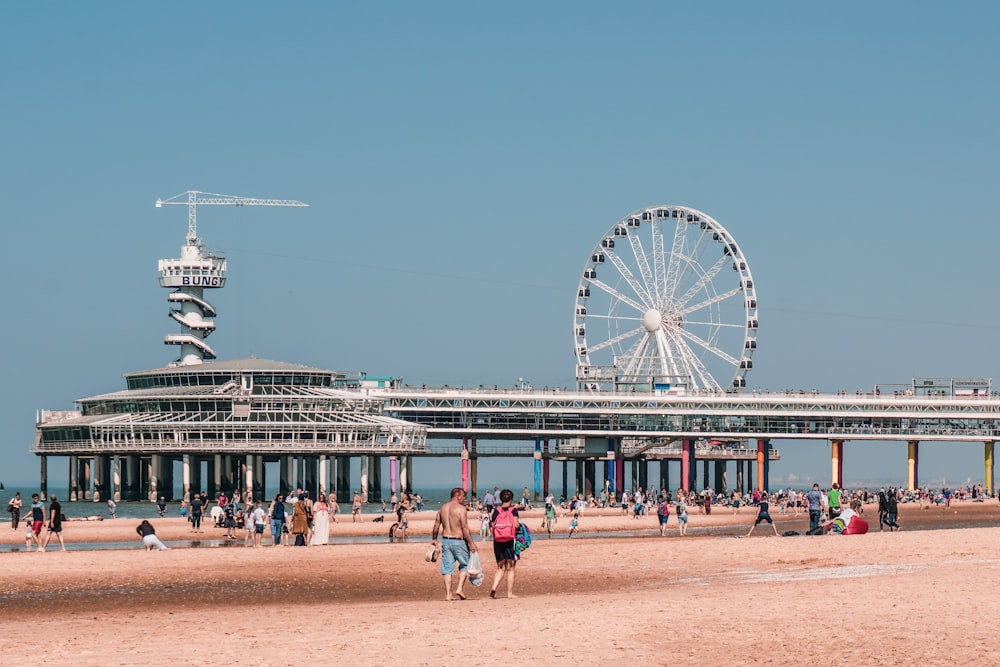 people walking on a beach with a ferris wheel in the background