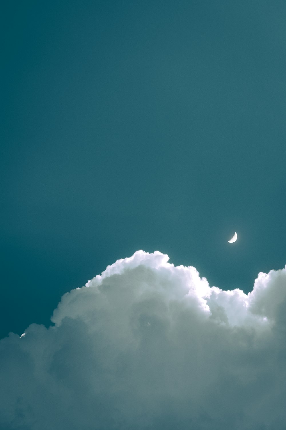 a plane flying through a cloudy sky with the moon in the distance