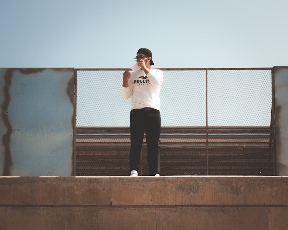 a man standing on top of a cement wall talking on a cell phone