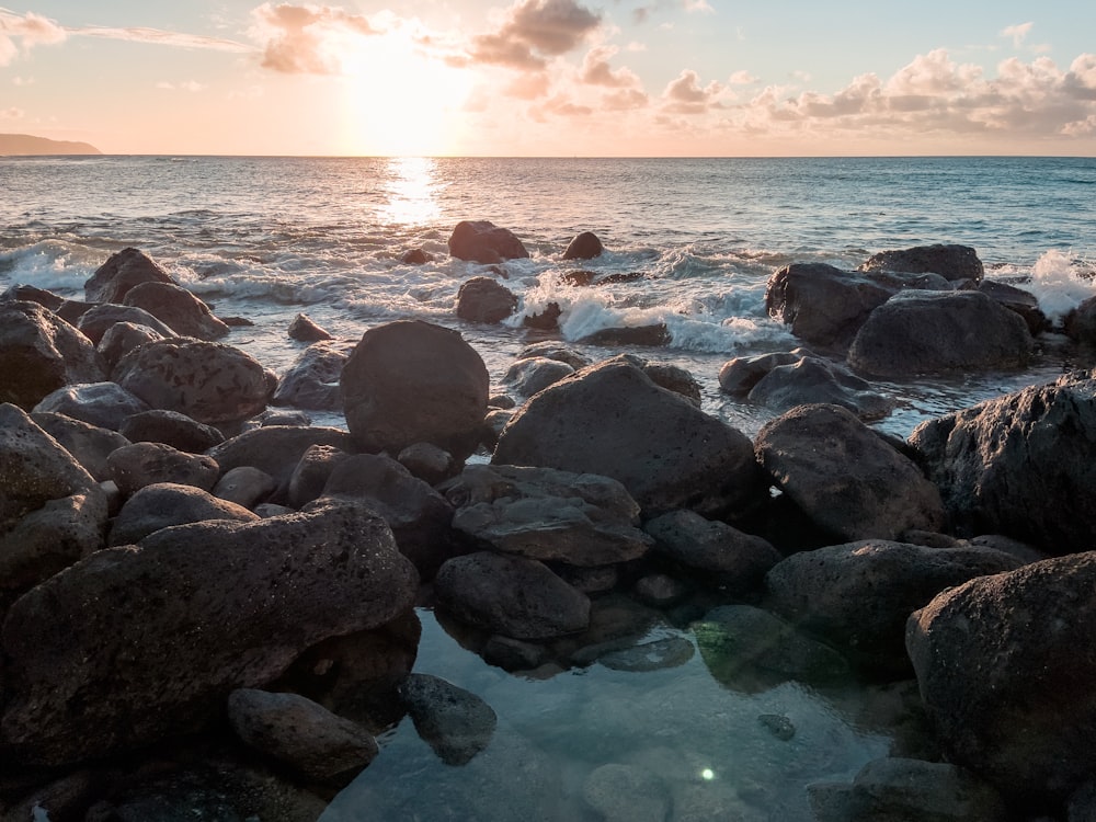 the sun is setting over the ocean and rocks