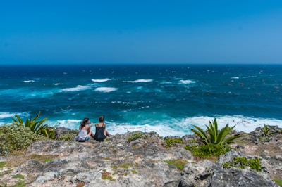 two people sitting on a rock overlooking the ocean