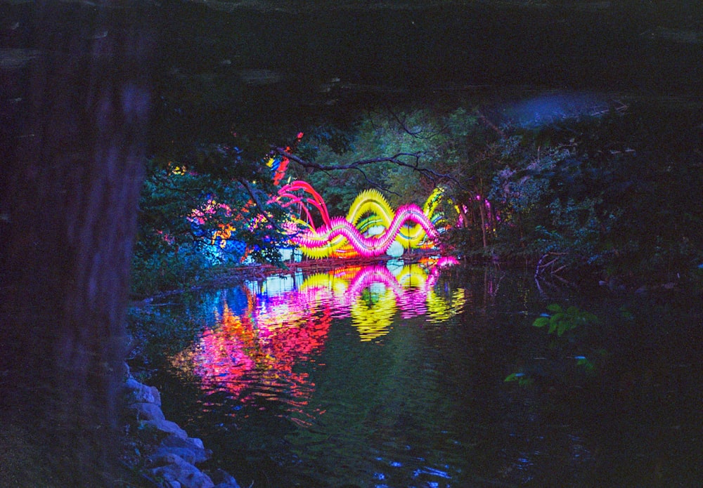 a pond filled with lots of colorful lights next to a forest