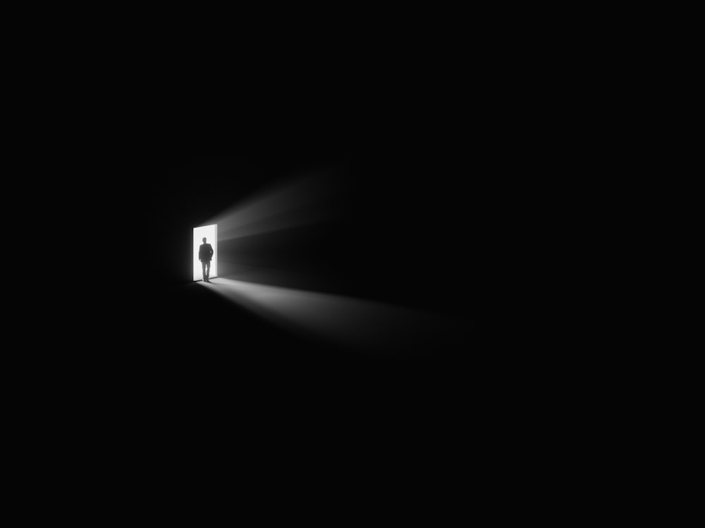 uma pessoa de pé em uma porta com uma luz que vem através dela