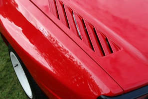Close-up of a freshly polished red sports car hood reflecting sunlight