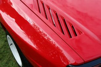Close-up of a freshly polished red sports car hood reflecting sunlight