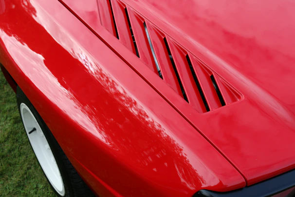 Close-up of a freshly painted vibrant red sports car hood gleaming in the sunlight.