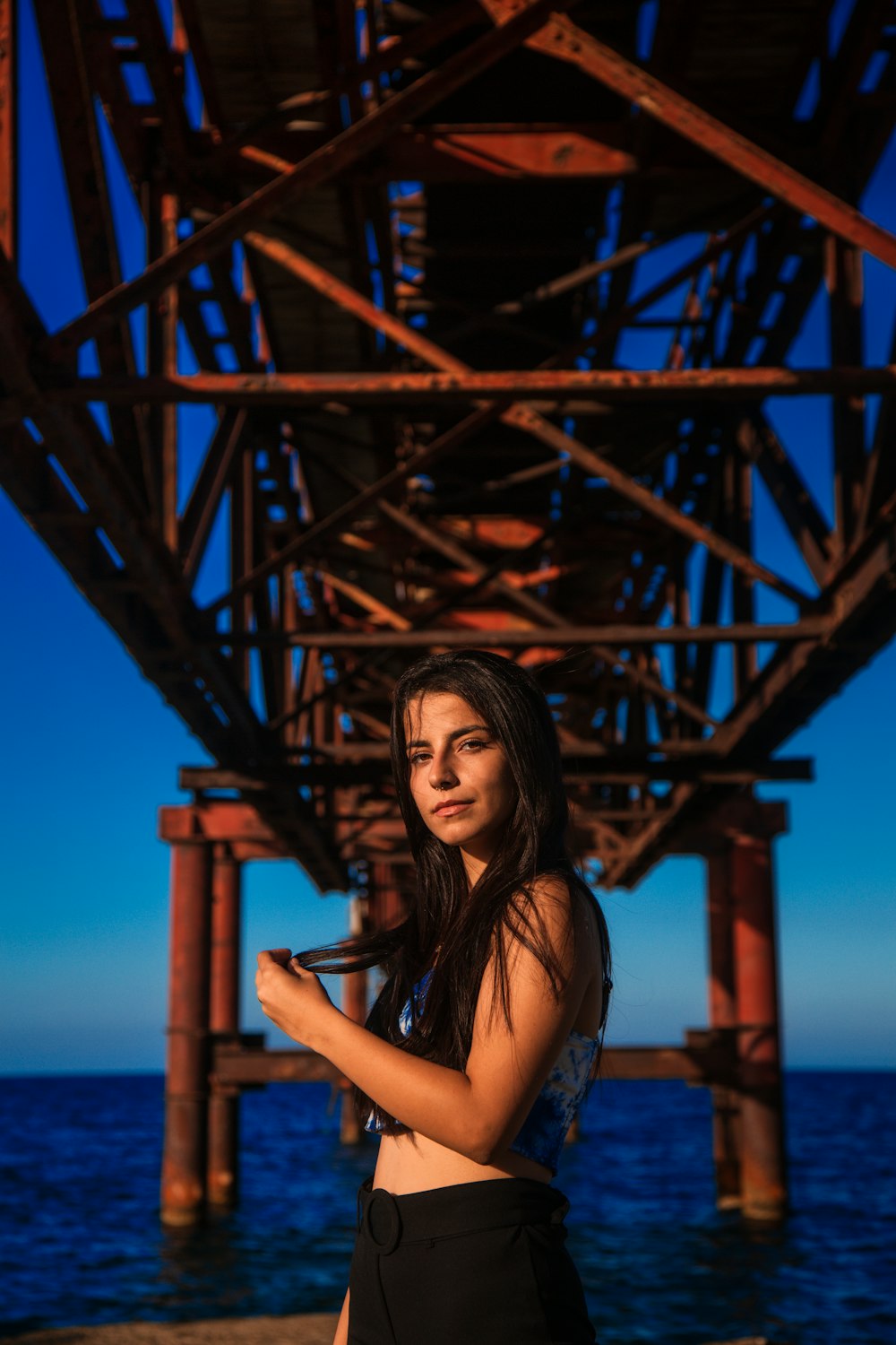 a woman standing under a bridge next to the ocean