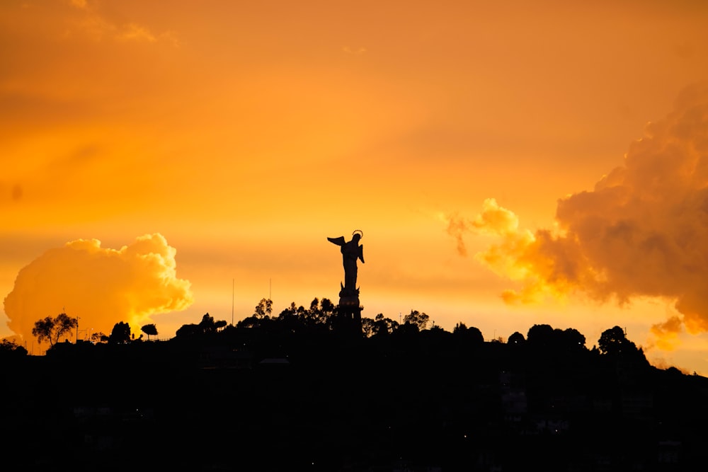 a statue is silhouetted against an orange sky