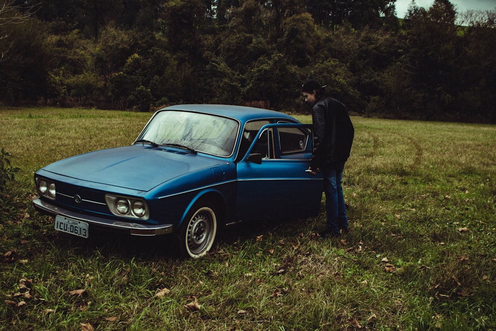a man standing next to a blue car in a field