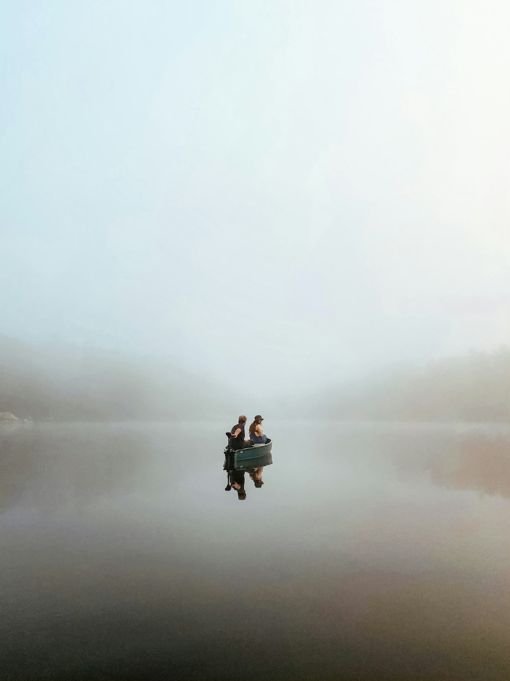 two people in a small boat on a foggy lake