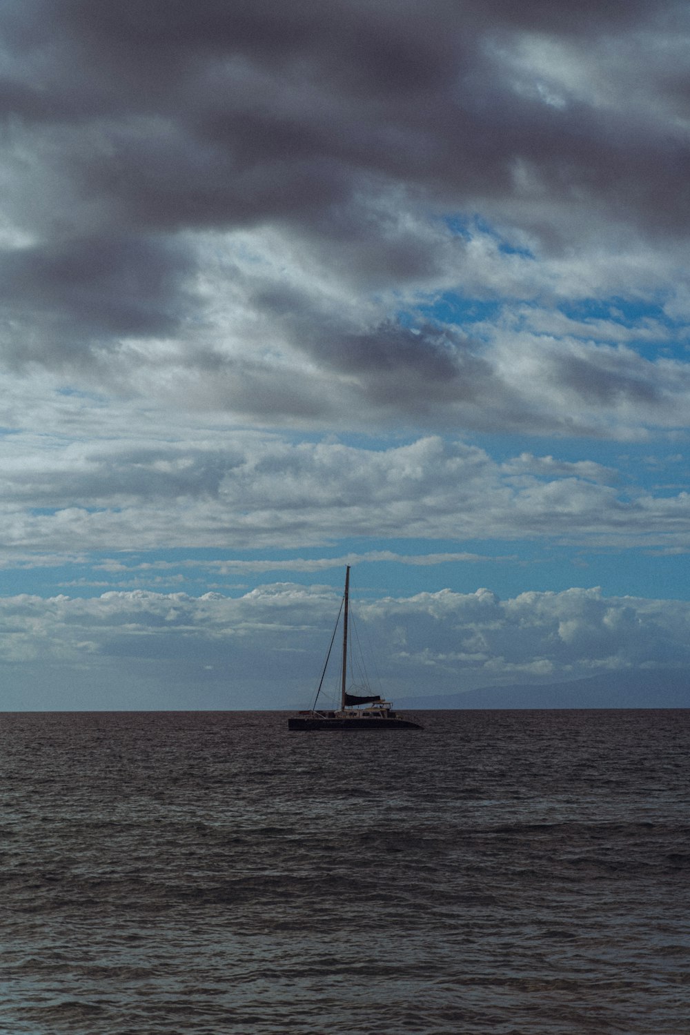 a sailboat in the middle of the ocean under a cloudy sky