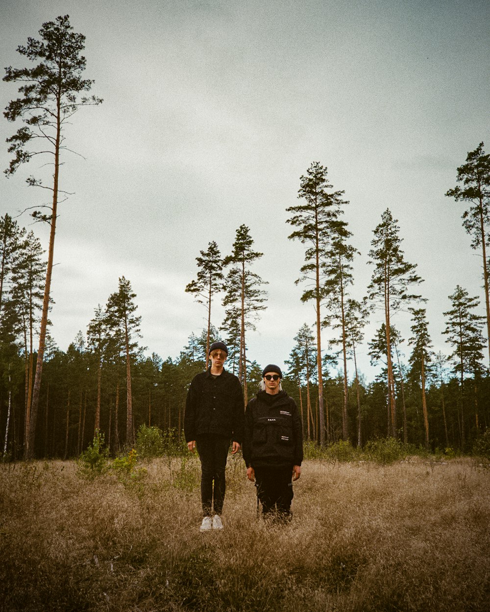 two people standing in a field with trees in the background