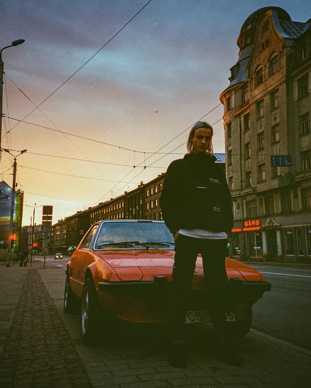 a man standing next to a red car on a street