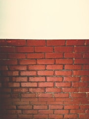 A section of a red brick wall is topped by a plain white surface. The bricks are arranged in horizontal layers with visible mortar lines, giving a textured and rustic appearance.