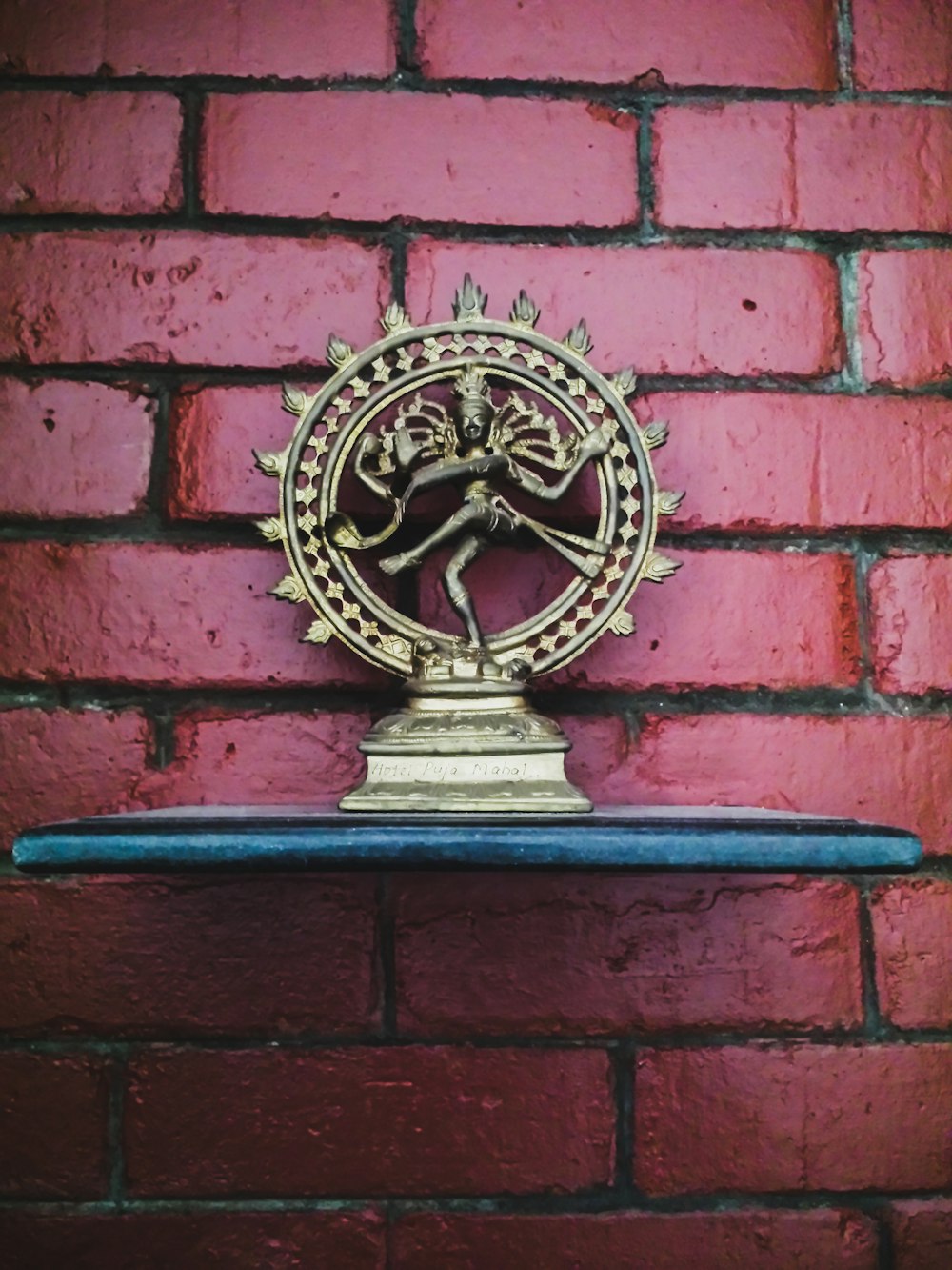 a brass statue on a shelf against a red brick wall