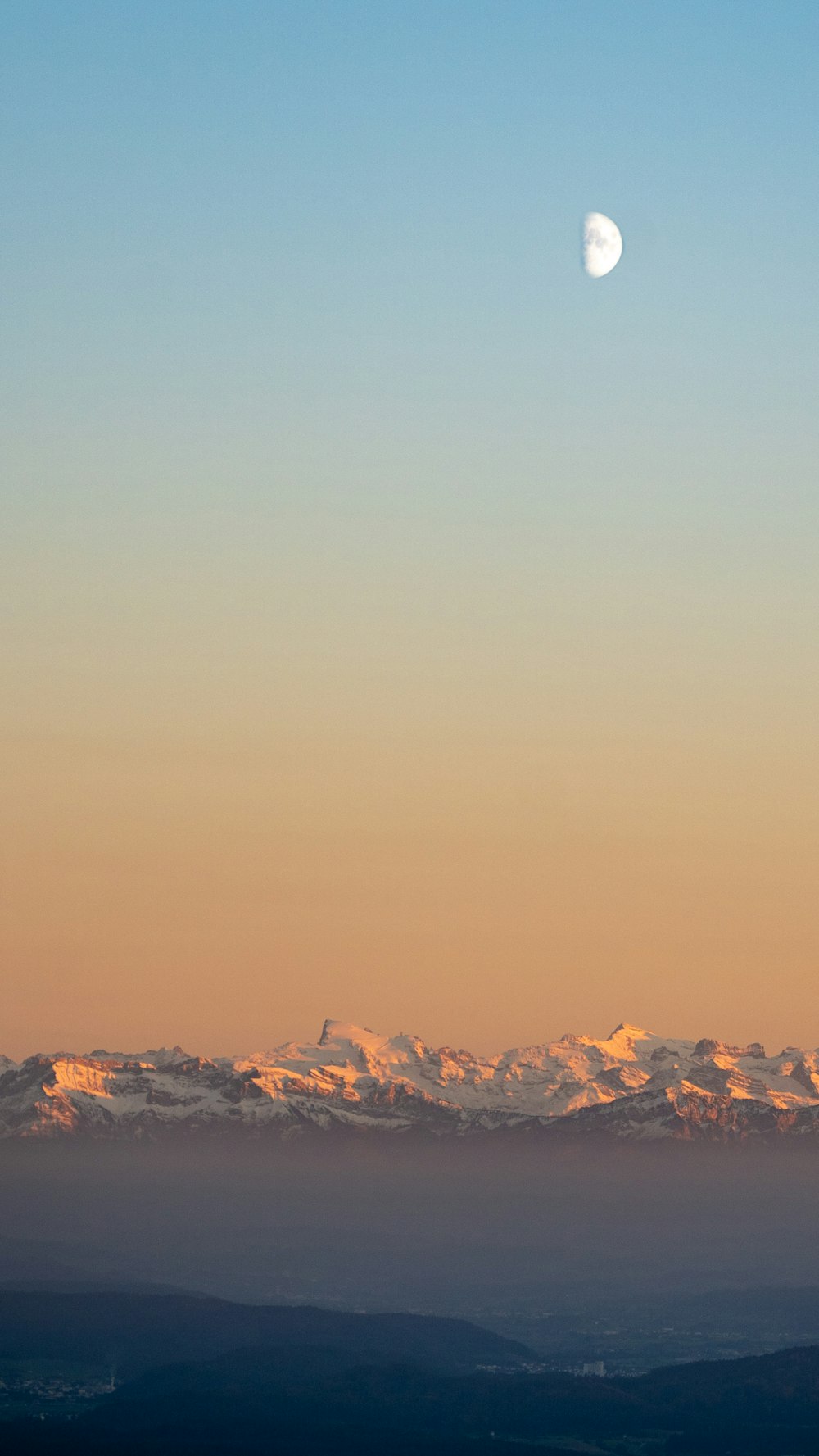 Una vista de una cadena montañosa con media luna en el cielo