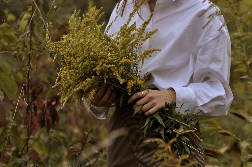 a woman in a white shirt holding a bunch of plants