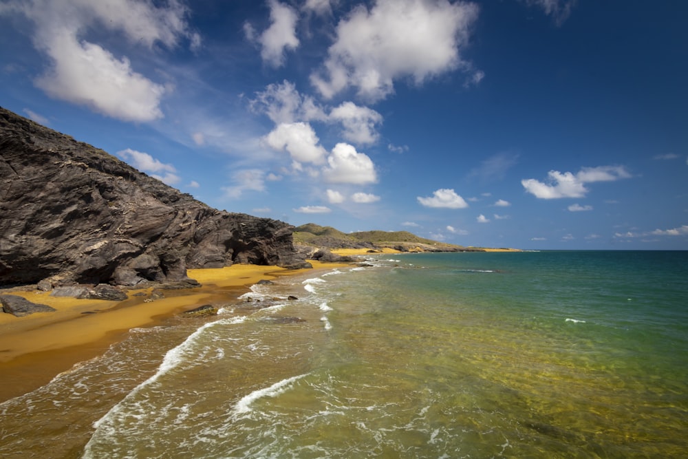 a sandy beach next to the ocean under a cloudy blue sky