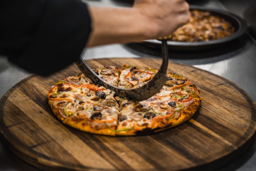 a person cutting a pizza with a pizza cutter