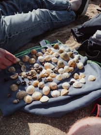a person sitting on the ground with a bunch of seashells on a towel