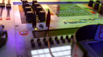 A close-up view of an audio mixing console with multiple knobs, sliders, and cables. The surface features a reflective panel with the brand name 'NIROMC'. The lighting casts a colorful glow, highlighting the controls and giving a futuristic feel.