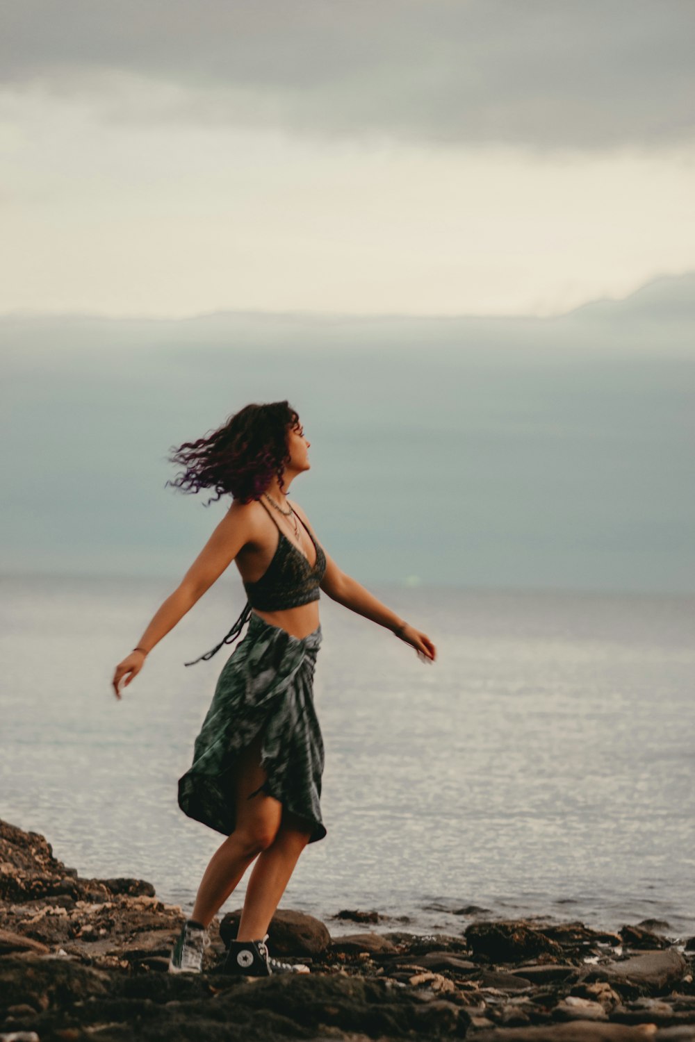 a woman standing on a rocky beach next to the ocean