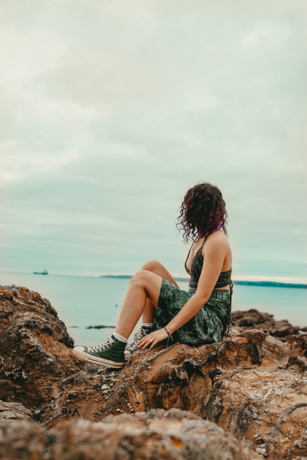 a woman sitting on a rock near the ocean