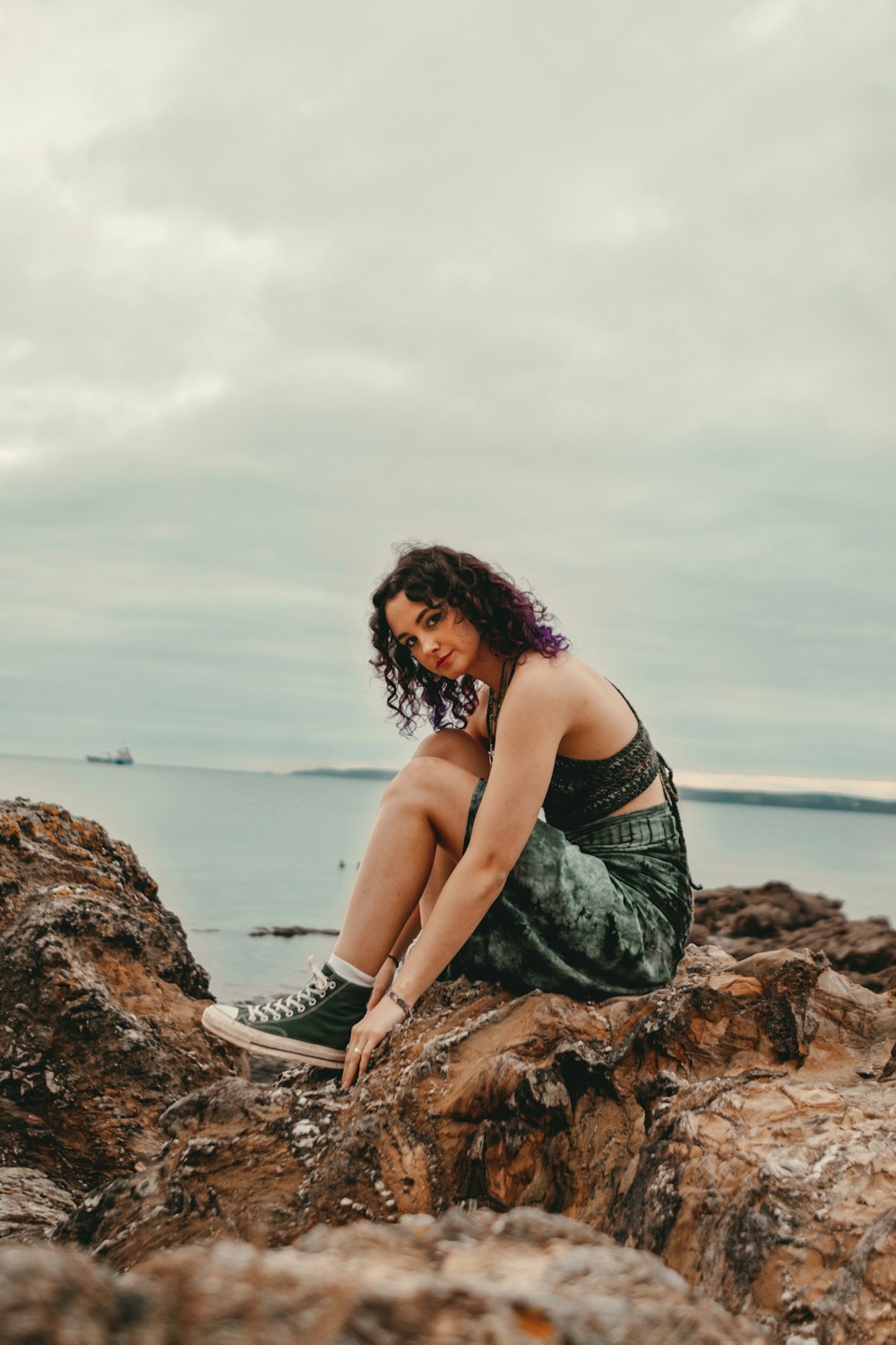a woman sitting on a rock near the ocean
