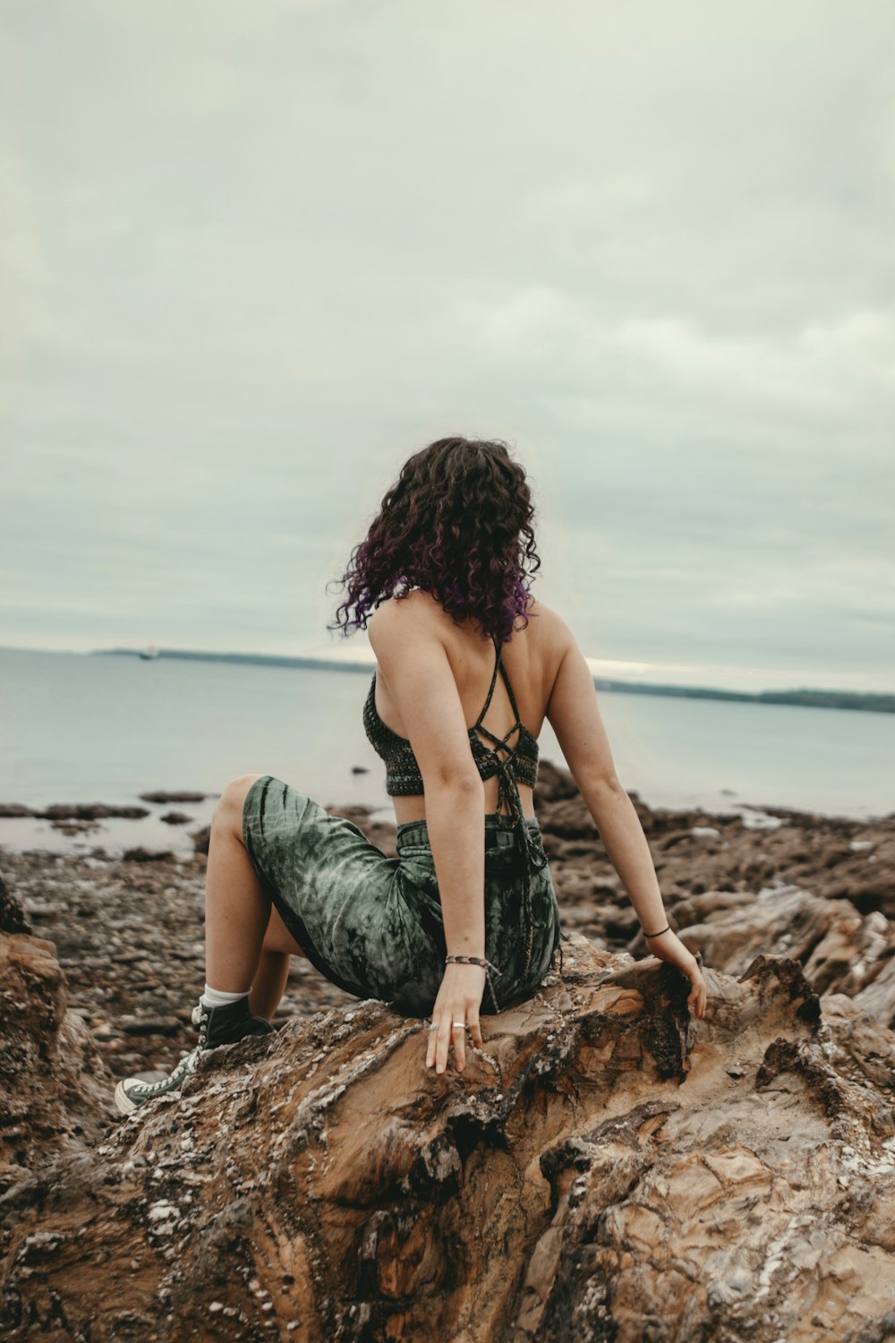 a woman sitting on top of a rock next to the ocean