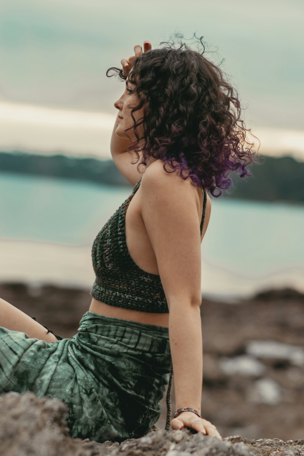 a woman sitting on top of a rock near the ocean