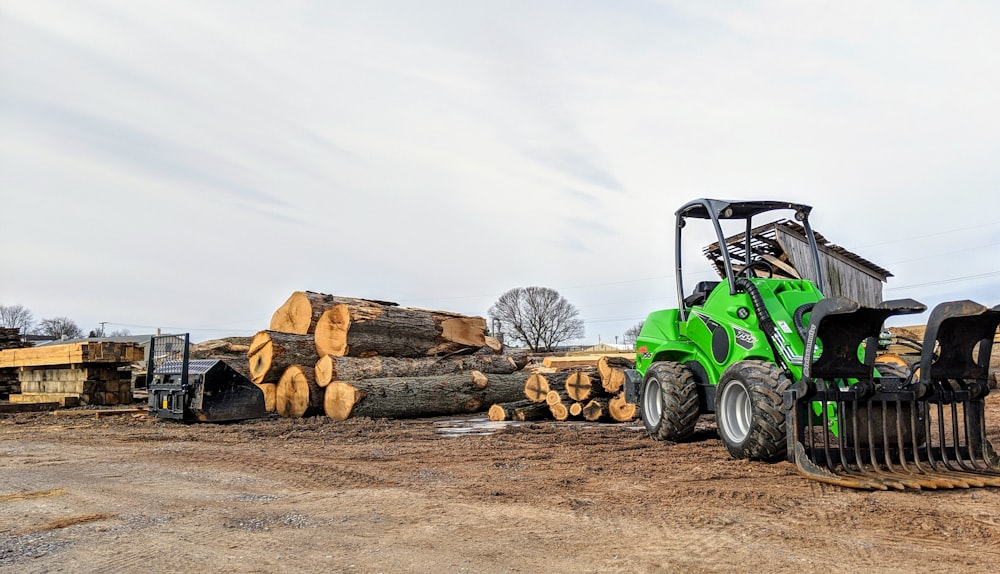 a green tractor parked next to a pile of logs