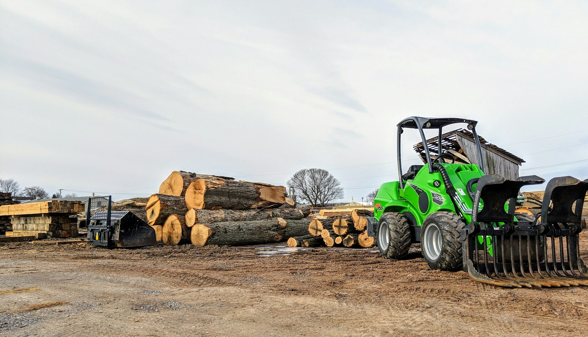 a green tractor parked next to a pile of logs