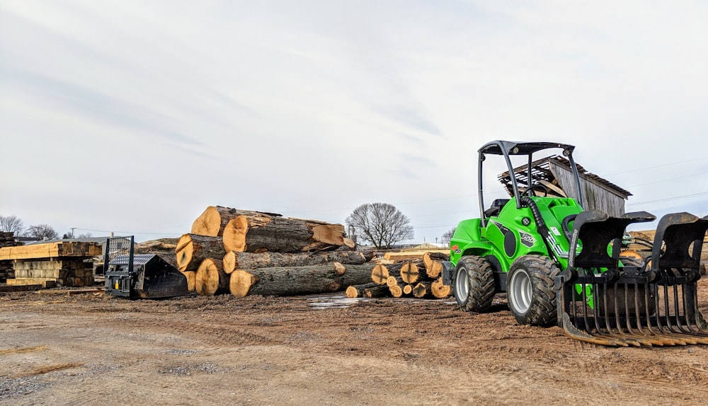 Ein grüner Traktor parkt neben einem Stapel Baumstämme