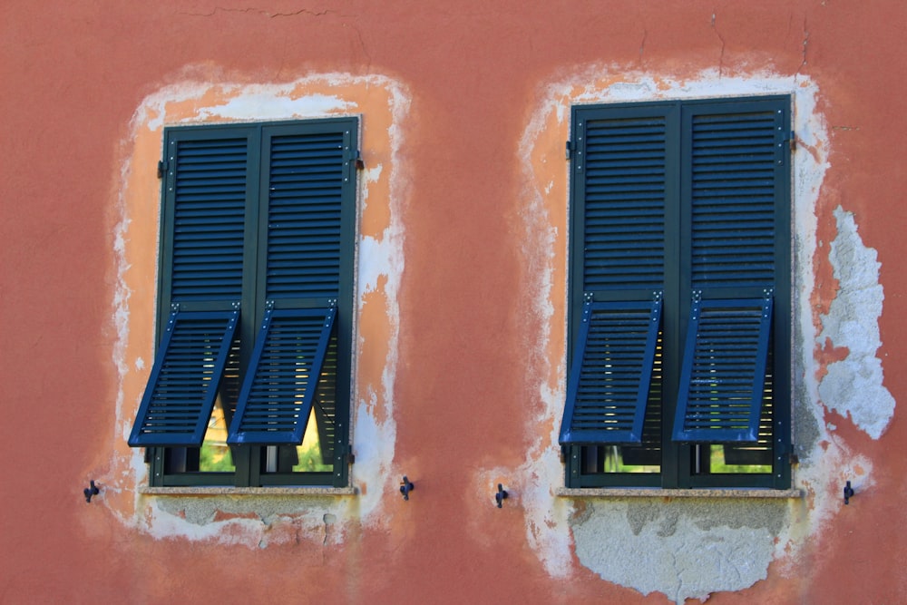 two windows with blue shutters on a red wall