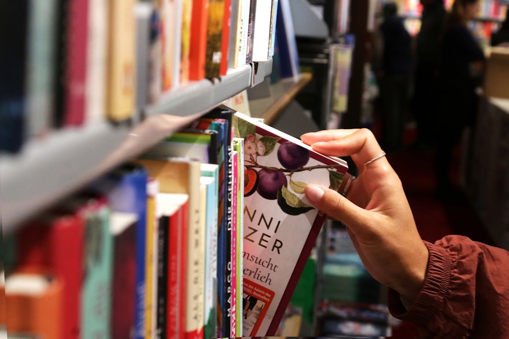 a person picking up a book from a book shelf