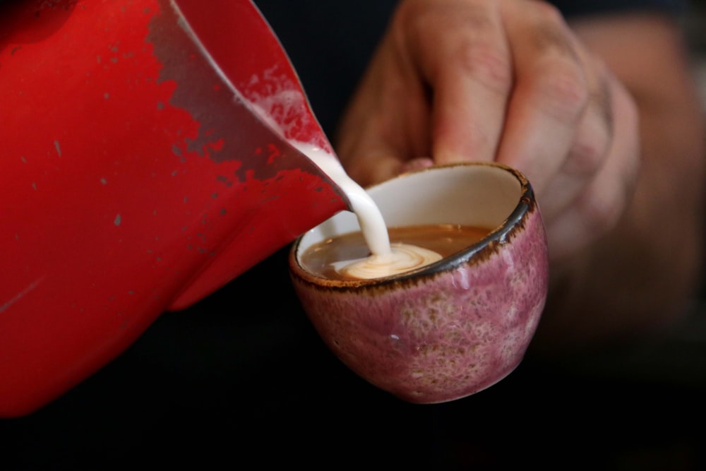 a person pouring milk into a red cup