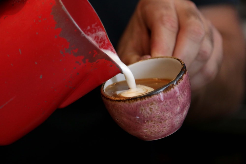 una persona vertiendo leche en una taza roja