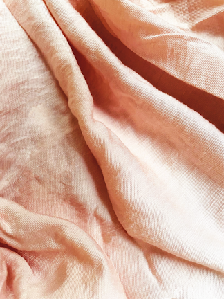 A close-up view of a piece of fabric with soft and delicate folds, displaying a mix of textures. The material appears lightweight and finely woven, with subtle variations in shading due to the way the light hits the surface.