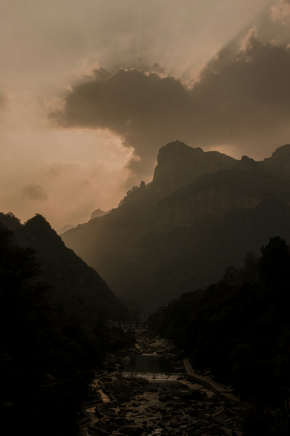 a river running through a lush green valley under a cloudy sky