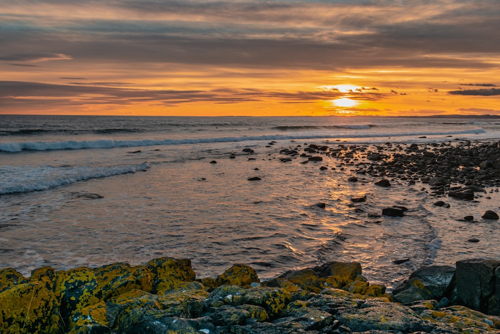 the sun is setting over the ocean and rocks