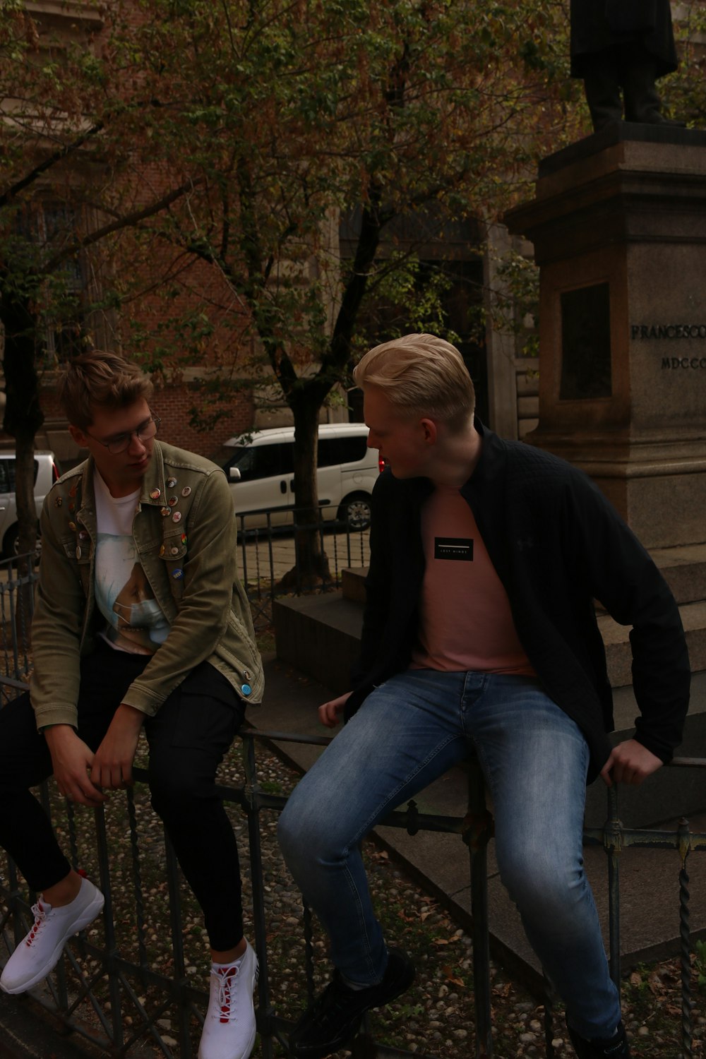 two young men sitting on a fence in front of a statue