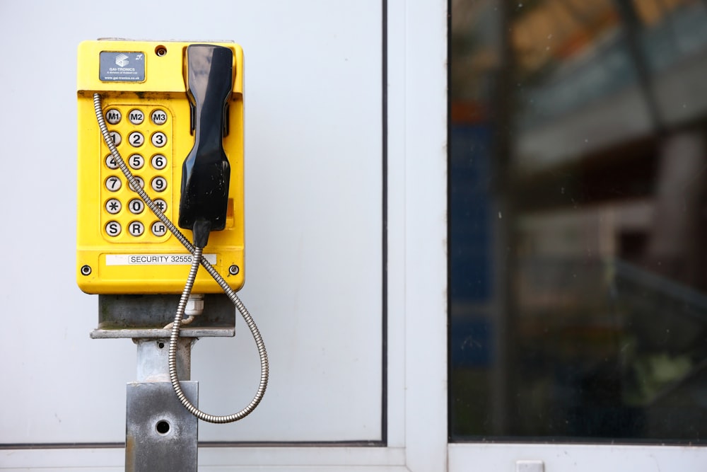 a yellow phone sitting on top of a metal pole